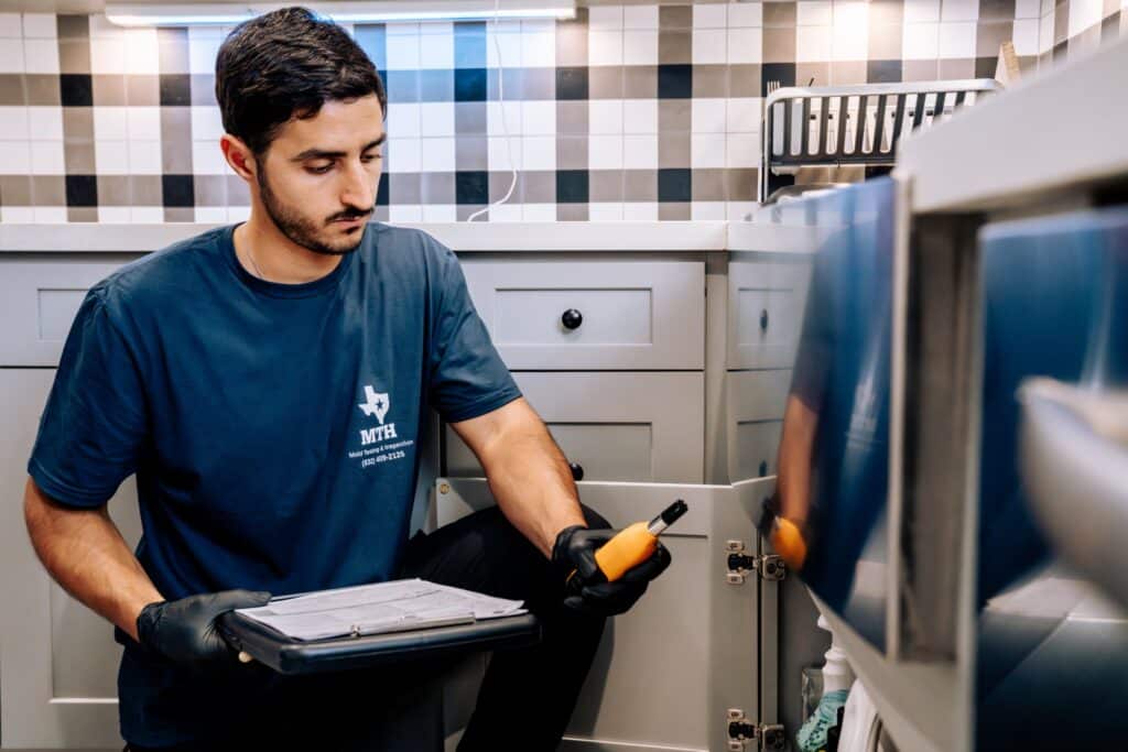 Mold assessor inspecting under-sink plumbing for moisture and hidden mold in a Houston kitchen