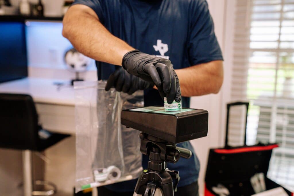 Gloved hand placing a spore trap cassette beside an air sampling pump before sealing samples for the lab