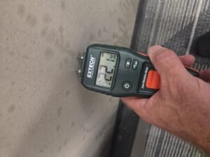 Moisture meter reading on a stained office wall during a commercial mold inspection in Pearland
